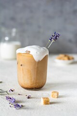 A glass of coffee with ice, milk (cream) and lavender flowers on a light background. Cold summer drink, Iced coffee.