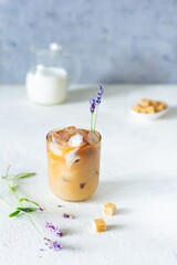 A glass of coffee with ice, milk (cream) and lavender flowers on a light background. Cold summer drink, Iced coffee.