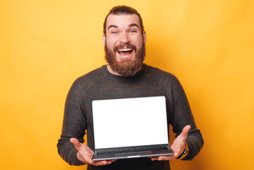 Amazed handsome bearded man showing white screen on laptop and smiling.