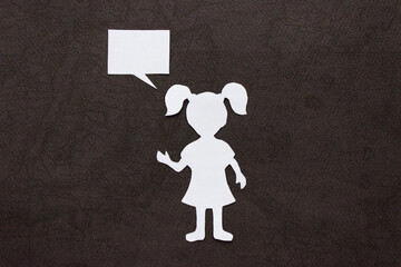 Silhouette of a girl in a dress and with ponytails made of white paper, cut by hand. In the center of the photo. On black background