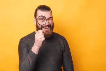 Photo of man looking trough magnifying glass over yellow background.