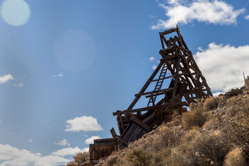 Fototapeta na wymiar Backlit wooden head frame against blue sky and clouds on a hill in the desert