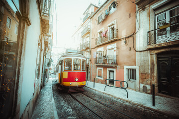Plakat A wide-angle view of a red retro tram on a narrow street with one-way rail traffic in a European city; a vintage tourist streetcar in yellow and red colors on a tramway track over paving stone