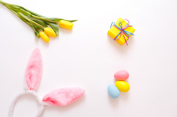 yellow tulips and colorful Easter eggs gift box, rabbit ears on a white background, top view.