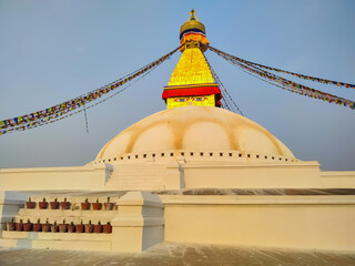 View of Boudhanath Stupa (or Bouddha Stupa) in the rays of the setting sun in Kathmandu city, Nepal. Prayer flags wings on the wind. No people. Religious architecture theme.