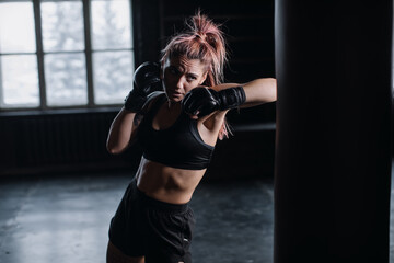 cool female fighter in boxing gloves trains in the gym. Mixed martial arts
