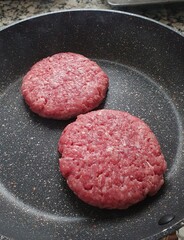 Two raw meat burgers, on a frying pan on the fire.  Concept of preparing food, cooking with ingredients, recipe books.