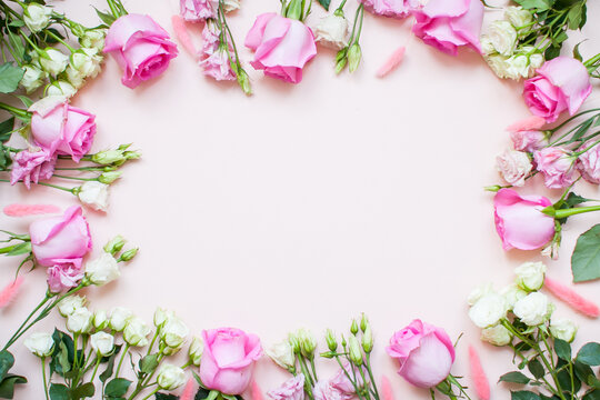 Frame of delicate white and pink roses and eustomas on a light pink background. Layout. Flat lay