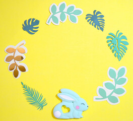 Frame for text with Easter bunny and paper leaves. Top view on yellow Easter background. Copyspace.