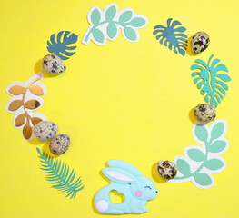 Frame for text with Easter bunny, quail eggs and leaves. Top view on yellow Easter background. Copyspace.