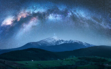 Arched Milky Way over the beautiful mountains with snow covered peak at night in summer. Colorful...