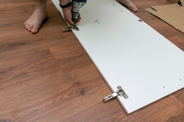 A man performs a professional assembly of flat furniture at home. Using the tools at hand.