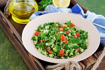Tabbouleh, parsley, tomato and cucumber vegetable salad with bulgur in a clay plate on an olive concrete background. Salad recipes. Healthly food.