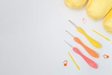 Top view of a set of colored crochet hooks laid out next to row counters and balls of yellow yarn. Colorful accessories for knitting on a gray background.Handmade craft recycle eco concept. Flat lay