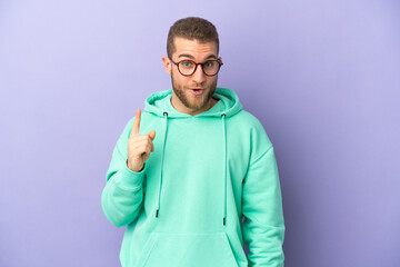 Young handsome caucasian man isolated on purple background intending to realizes the solution while lifting a finger up