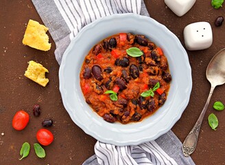 Large beans stewed with tomatoes, apple and bell peppers in a gray plate on a brown concrete background. Vegetarian and vegan food. Healthy eating.