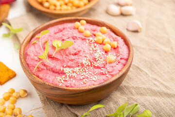 Hummus with beet and microgreen basil sprouts in wooden bowl on a white wooden background. Side view, selective focus.