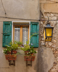 typical old Italian facade window with flowers and green shutters and lantern 