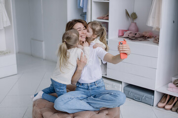 Young mother sits in a modern dressing room with a phone taking selfies with her twin daughters