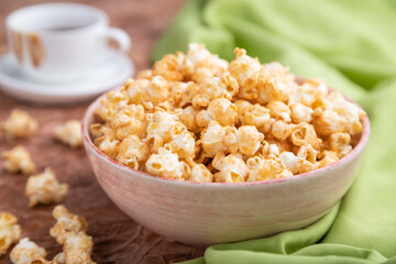 Popcorn with caramel in ceramic bowl on brown concrete background. Side view, selective focus.