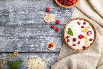Rice flakes porridge with milk and strawberry in wooden bowl on gray wooden background. Top view, copy space.