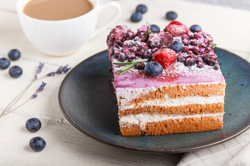 Berry cake with milk cream and blueberry jam on blue ceramic plate with cup of coffee and fresh blueberries on a white wooden background. side view, selective focus.