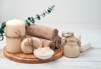 Fototapeta na wymiar Candles, soap and a set of brown towels with a branch of eucalyptus on a white wooden background. Spa care.