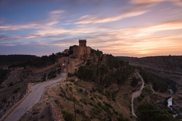 Landscape with the fortified city of Alarcon with its watchtowers and the castle on top of the hill in a colorful sunset, Cuenca, Spain