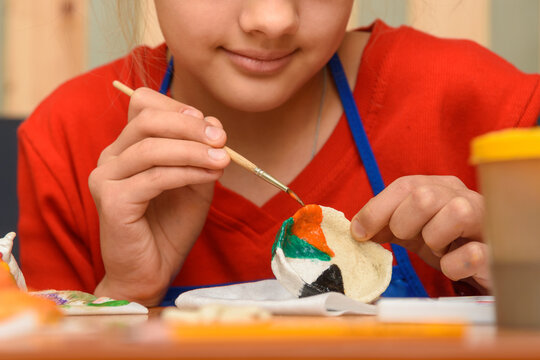 A girl paints a craft from salt dough with watercolors, close-up
