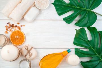 Oil, soap, towels, salt, candles and tropical leaves on a white wooden background. Top view.