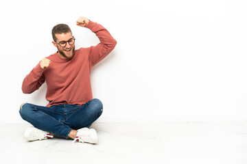 Young handsome man sitting on the floor celebrating a victory