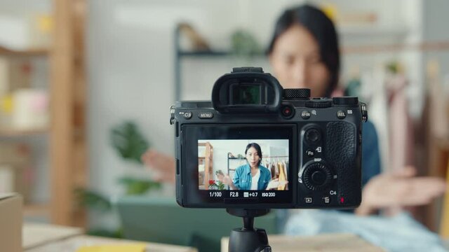 Young Asia lady fashion designer using mobile phone receiving purchase order and showing clothes recording video live streaming online at shop. Small business owner, online market delivery concept.