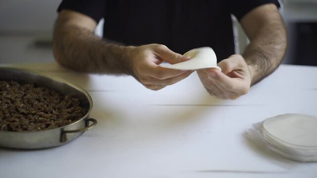 Male hands preparing an argentinean empanada over a white table. Putting the meat filling and closing it with a home made traditional repulgue.