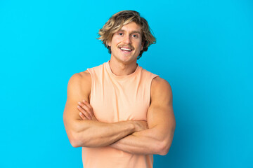 Handsome blonde man isolated on blue background keeping the arms crossed in frontal position