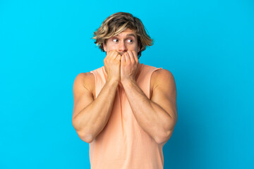 Handsome blonde man isolated on blue background nervous and scared putting hands to mouth