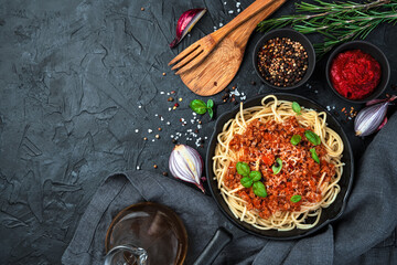 Hot dish with spaghetti and thick sauce on a black background. Top view, horizontal. The concept of cooking.
