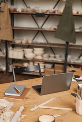 Vertical background image of laptop on wooden table in empty pottery workshop, small business concept, copy space