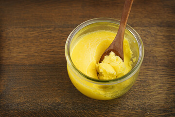  Homemade ghee in jar and wooden spoon .   Ghee is purified butter. 