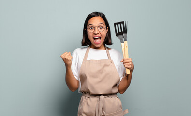 young hispanic woman feeling shocked, excited and happy, laughing and celebrating success, saying...