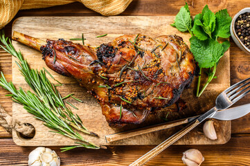 Roasted goat leg with herbs. Farm meat. Wooden background. Top view. Copy space