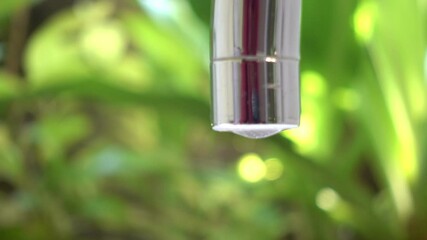 Crystal clear drops of water falling slowly from old brown pipe outdoors. Rusty tap needs reparing. Close-up stream of water splashing on blurred background. Pure water for people hygiene