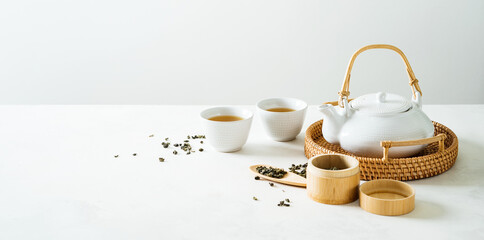 Asian tea concept mockup, two white cups of tea and teapot surrounded with green dry tea  with space for a text on light background. Wide banner. - obrazy, fototapety, plakaty
