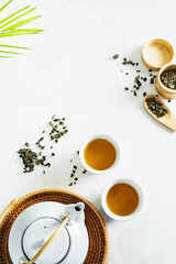 Plakat Asian tea concept, two white cups of tea and teapot surrounded with green tea dry leaves view from above, space for a text on white background