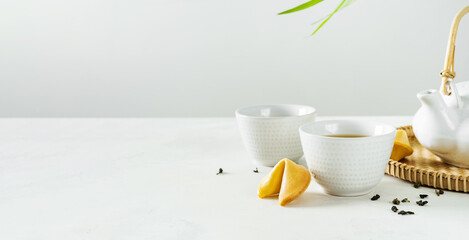 Asian  lifestyle mockup tea concept, two white cups of tea and teapot surrounded with green dry tea  with space for a text on light background. Wide banner.