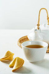 Tea in white Asian cup with fortune cookies on light background with copyspace.