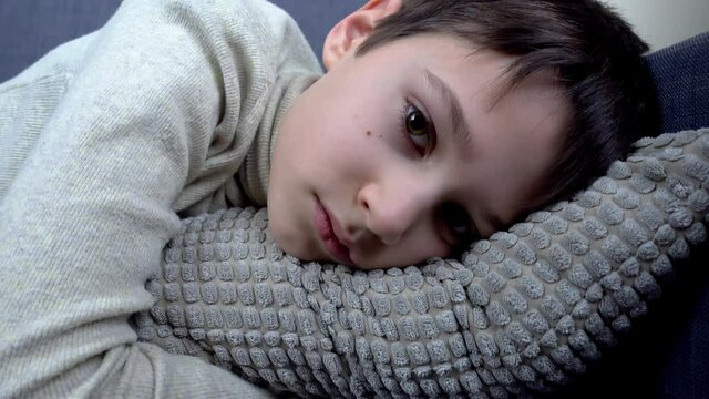 Young boy lying on couch at home. Child looking direct to the camera. 4k video footage
