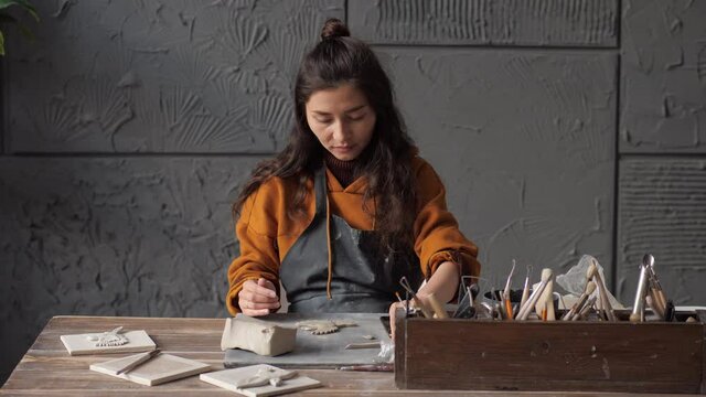 Young asian potter woman working on details of a clay handcraft piece. Work with different pottery tools. Start up small business, artwork and interior. Concept of creative leisure time and ceramics.