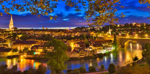 Fotobehang Panorama cityscape of old town of Bern with cathedral tower and Nydeggbr cke bridge illuminated at night reflecting into Aare river. Popular landmark of historical town UNESCO World Heritage Site. © bennymarty