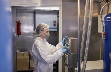 Side view portrait of young female worker pushing buttons at control panel while operating machines...