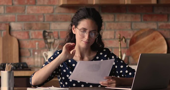 Businesswoman sit at table in kitchen at quarantine work at home, hold document report makes market research, review business strategy, learn sales results in graphs and charts, do paperwork concept